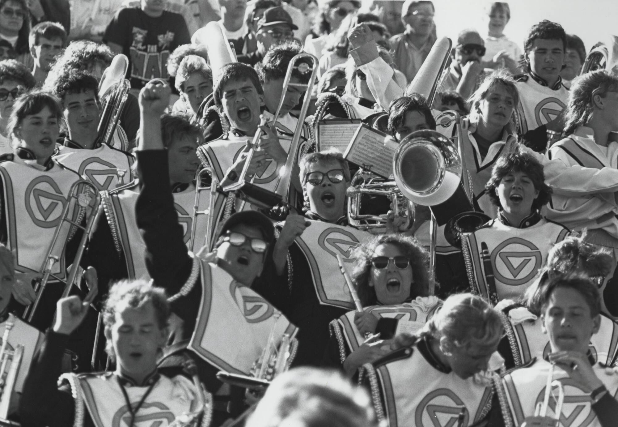 The laker marching band circa 1989, in the stands cheering. One student is raising their fist to the sky.